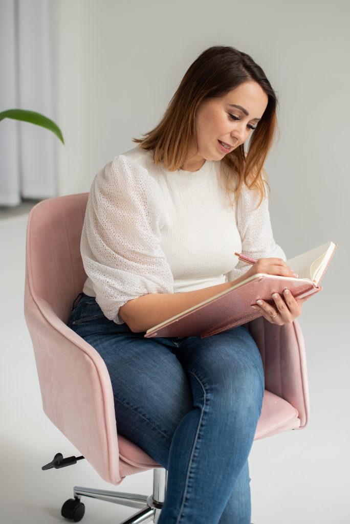 Karen sentada en una butaca rosa, escribiendo en una libreta